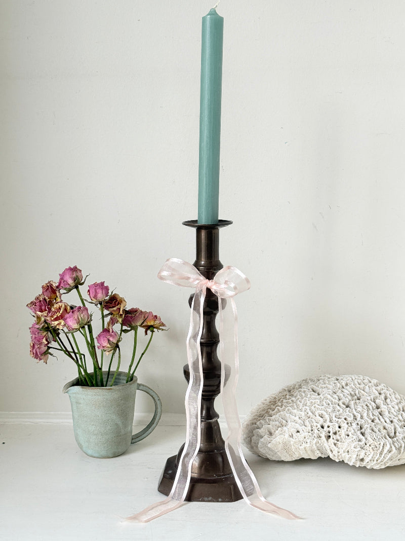 Bronze coloured vintage candlestick with bobbin stem and shaped base styled with taper candle on white surface