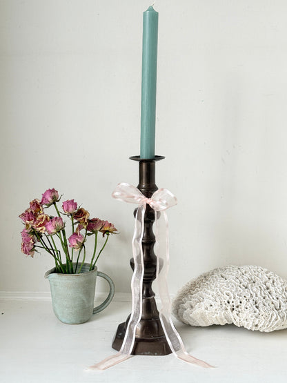 Bronze coloured vintage candlestick with bobbin stem and shaped base styled with taper candle on white surface