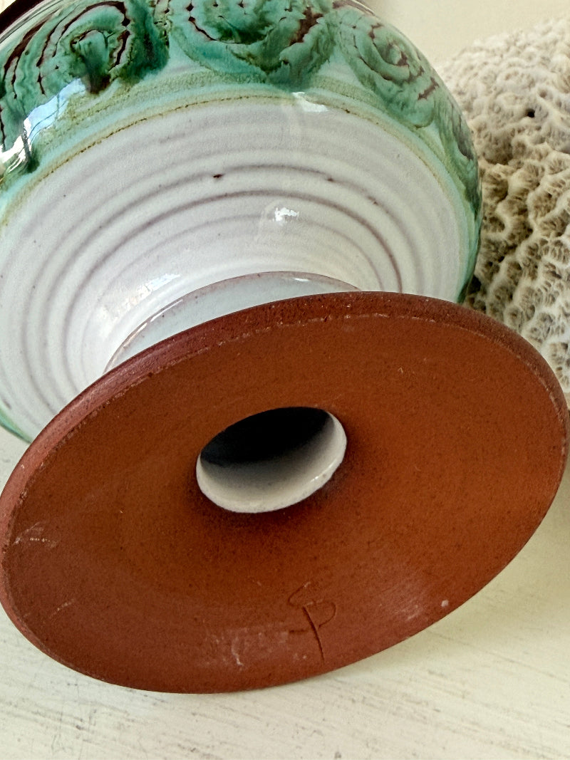Hand thrown studio pottery footed bowl with green and brown swirling decoration photographed on a white surface