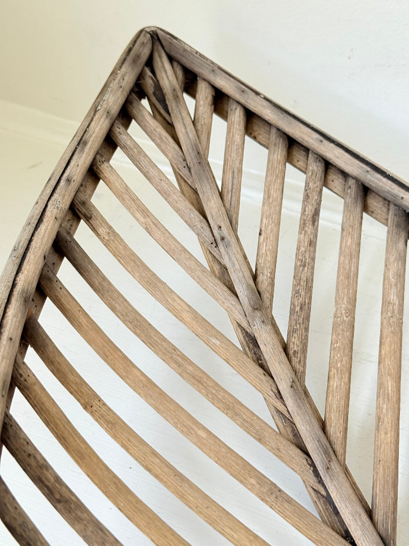 Large curved woven basket with slatted sides and repaired plywood base photographed on a white surface