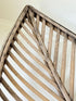 Large curved woven basket with slatted sides and repaired plywood base photographed on a white surface