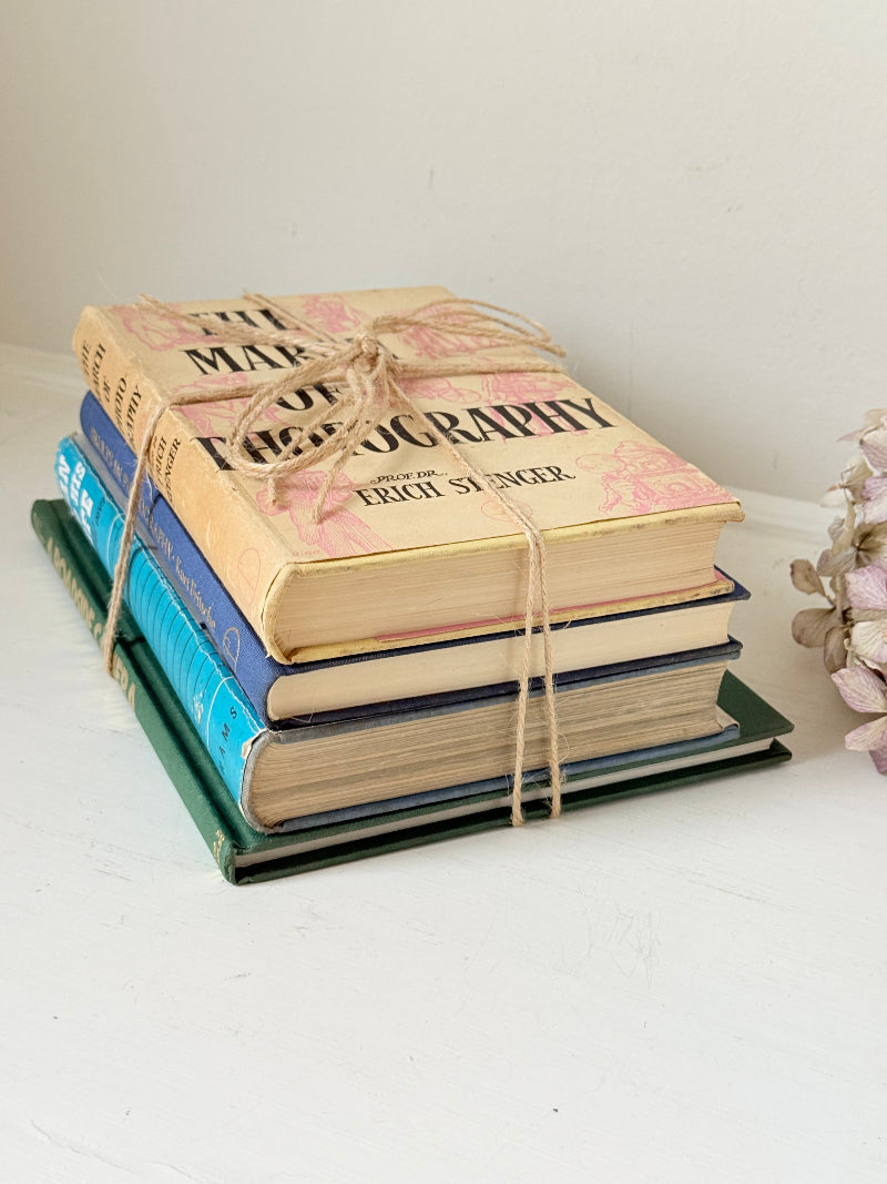 Bundle of vintage books in blue and neutral tones tied with twine, photographed on a white surface