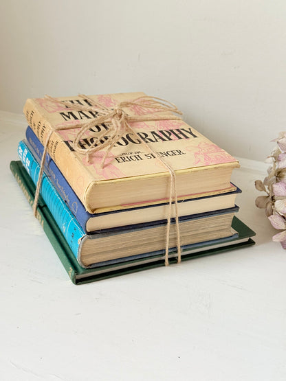 Bundle of vintage books in blue and neutral tones tied with twine, photographed on a white surface