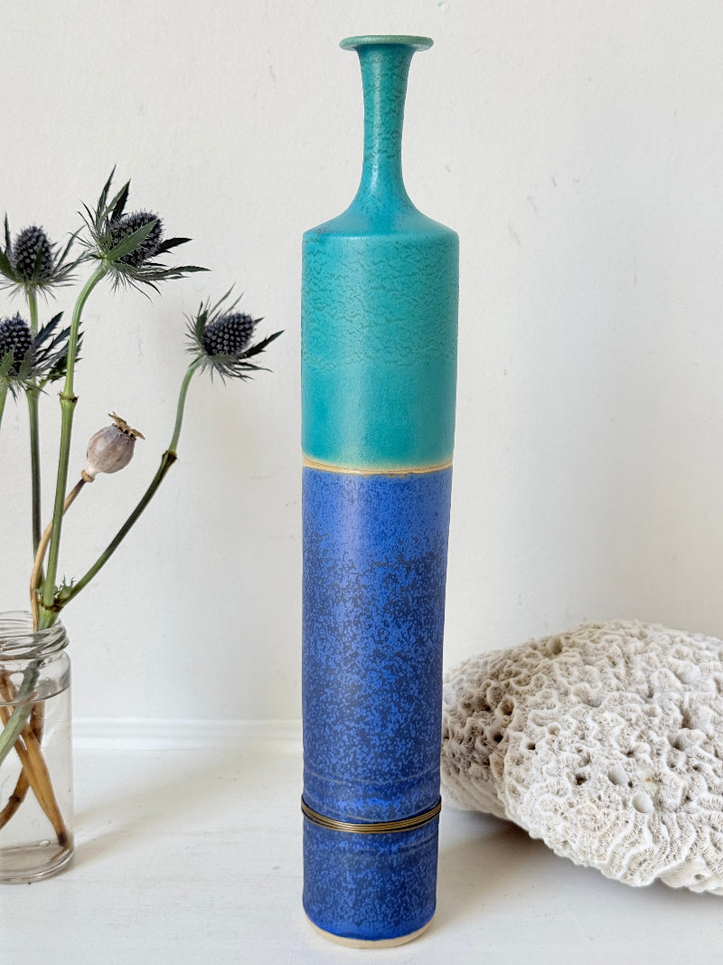 Tall vintage studio pottery bottle vase in turquoise and cobalt blue glaze, photographed on a white surface