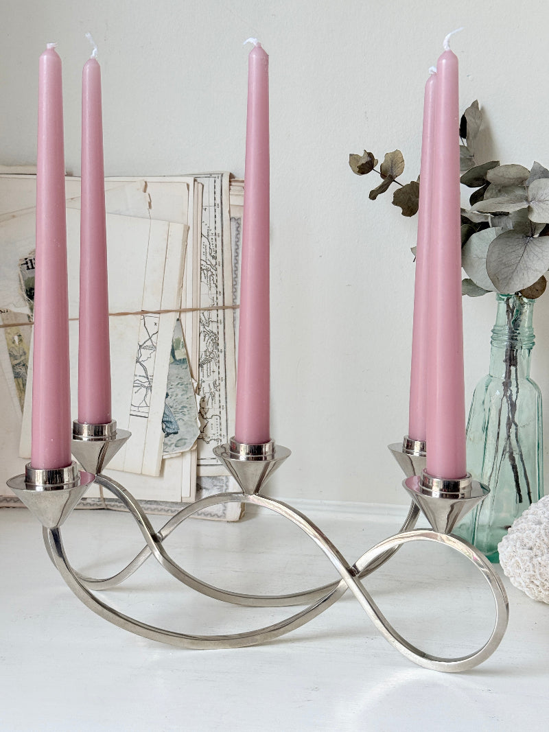 Silver tone five light candelabra with a sculptural looped base holding pink candles, photographed on a white surface