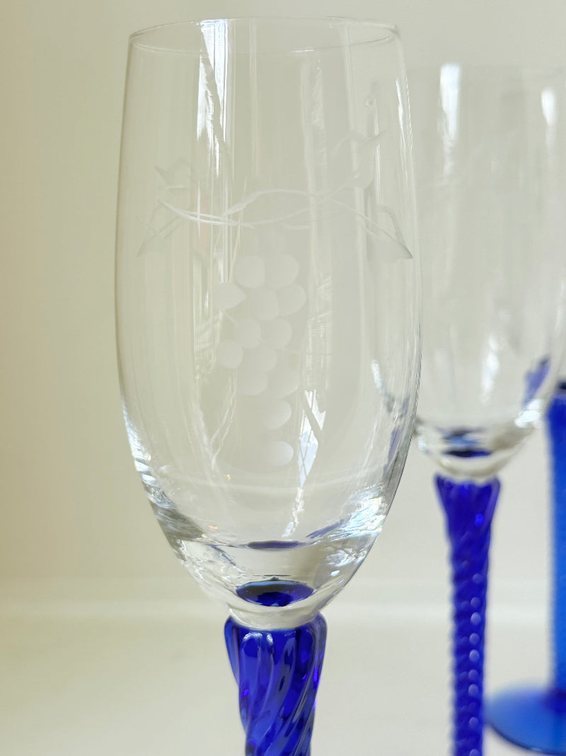 Set of six vintage French champagne flutes with tall clear bowls and cobalt blue twisted stems, photographed on white surface.