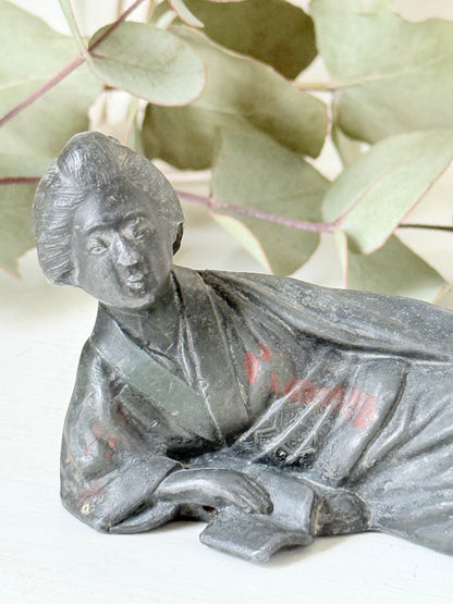 antique japanese bronze reclining lady with impressed marks to base photographed on white surface with foliage background