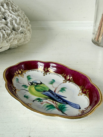 Vintage hand painted bird trinket dish with pink border and gilt detail photographed on a white surface