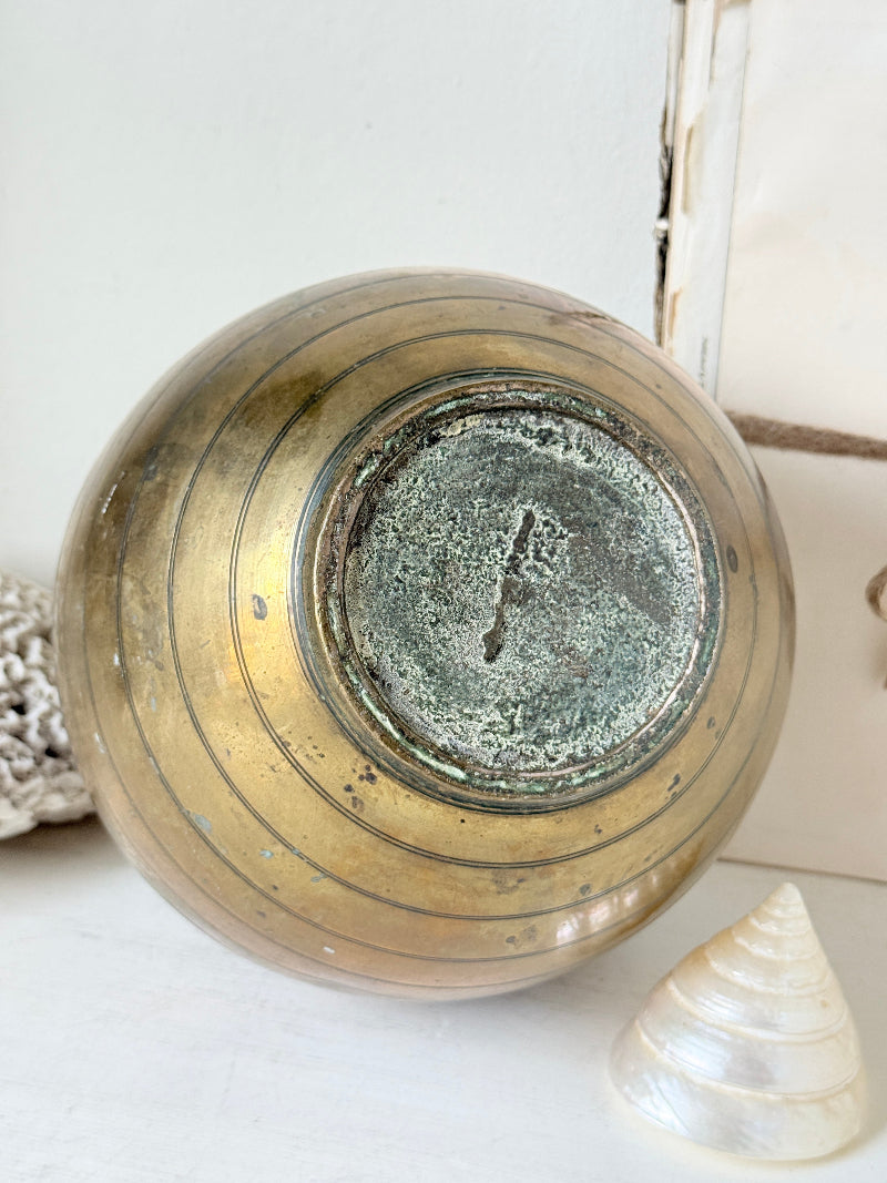 A vintage round ceramic vase with a distressed metallic gold finish and concentric ring details, shown from a top-down angle on a white surface with seashells nearby.