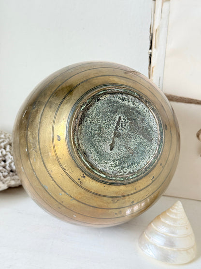 A vintage round ceramic vase with a distressed metallic gold finish and concentric ring details, shown from a top-down angle on a white surface with seashells nearby.