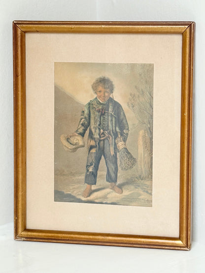 Vintage print of Little Beggar Boy in muted colours, framed under glass in simple wooden frame, on white surface.