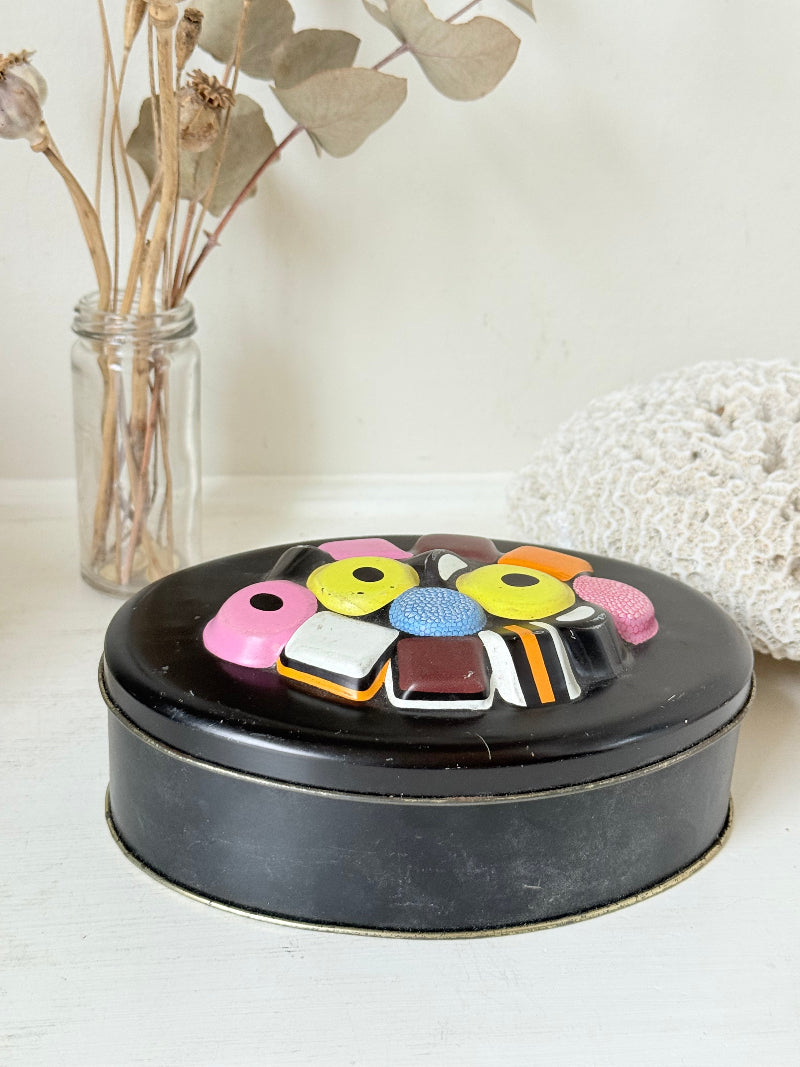 Vintage Liquorice Allsorts decorative tin with raised multicolour sweet design on black base, photographed on white surface.