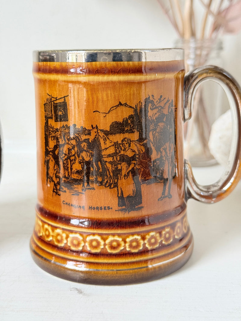 Pair of Ridgways stoneware tankard mugs photographed on a white surface in amber brown glaze with black Coaching Days and Coaching Ways transfer scenes