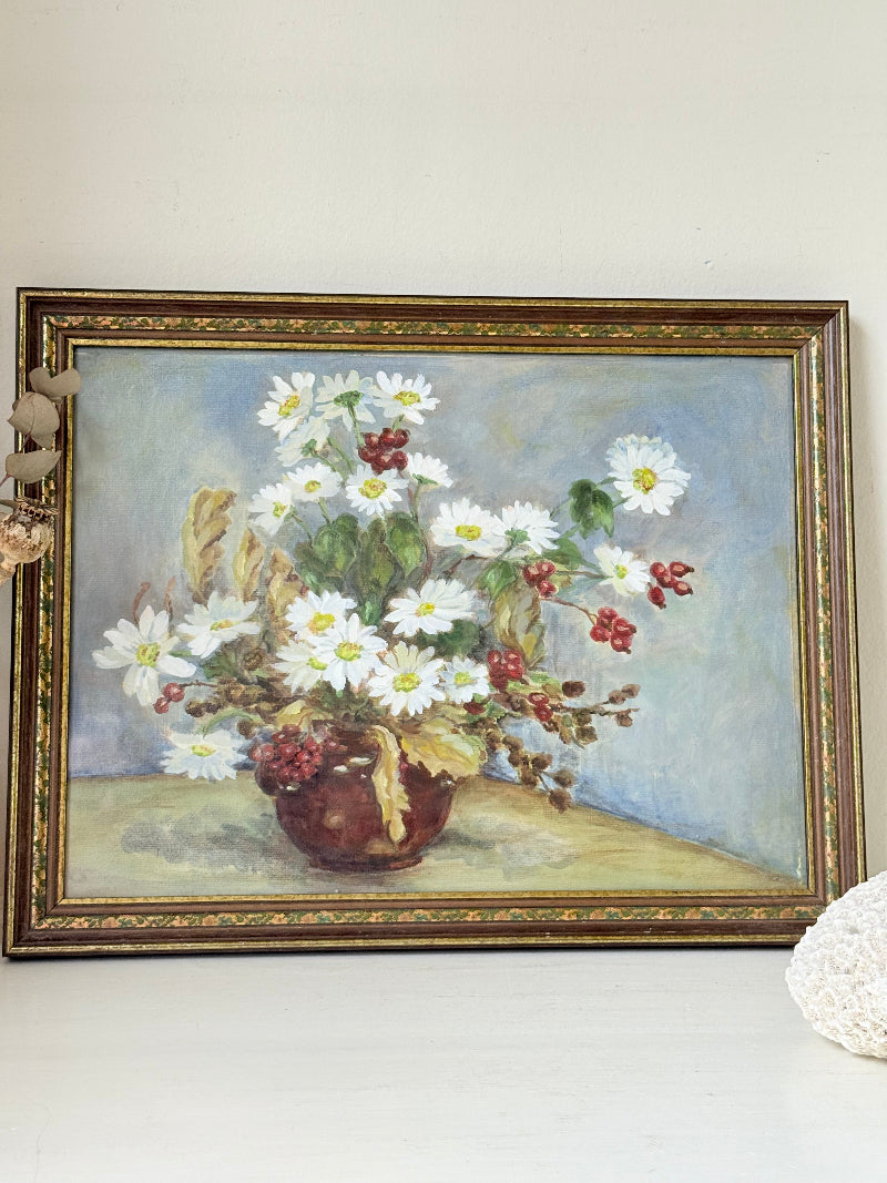 Vintage oil painting on board of daisies in a vase, framed under glass and photographed on a white surface beside dried flowers.