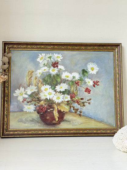 Vintage oil painting on board of daisies in a vase, framed under glass and photographed on a white surface beside dried flowers.