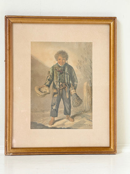 Vintage print of Little Beggar Boy in muted colours, framed under glass in simple wooden frame, on white surface.