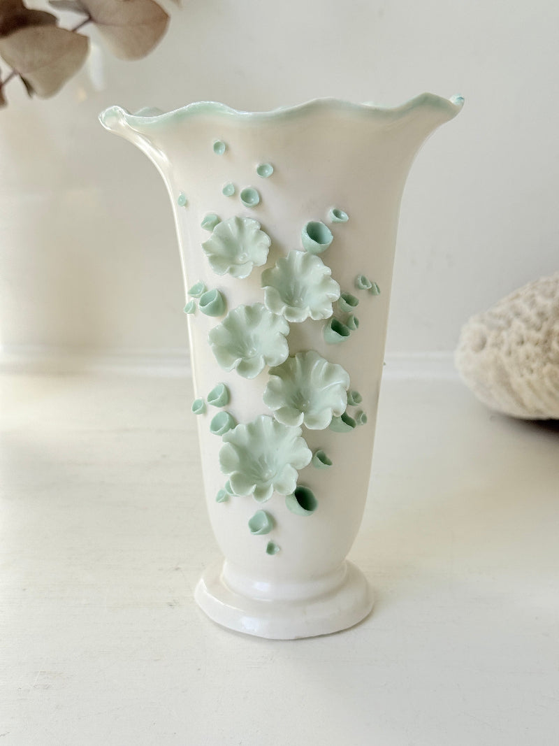 White Chessell Pottery studio vase with rippled rim and raised aqua floral decoration photographed on a white surface