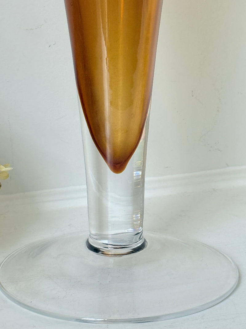 Tall mid-century amber trumpet vase with flared rim and clear glass foot, styled against a neutral background