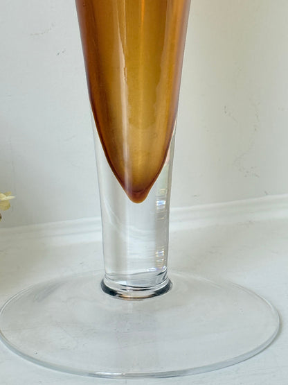 Tall mid-century amber trumpet vase with flared rim and clear glass foot, styled against a neutral background