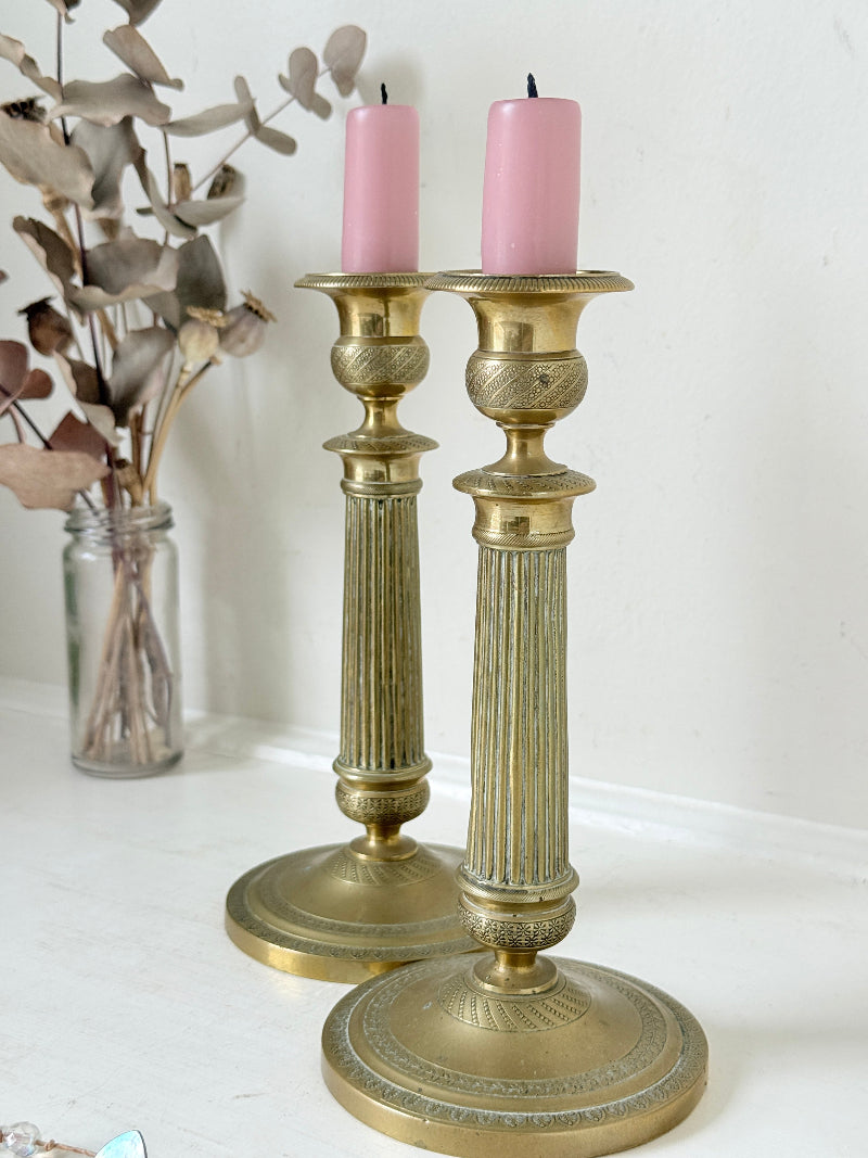 Pair of antique brass Empire style candlesticks photographed on a white surface with fluted columns and circular bases holding pink taper candles
