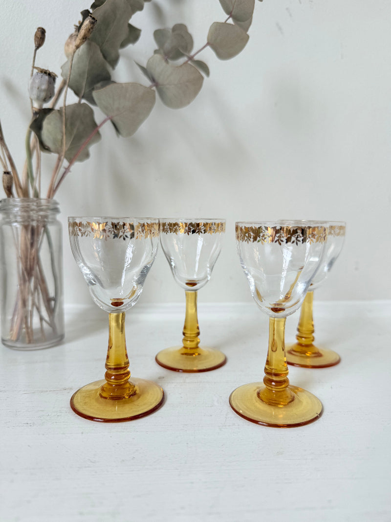 Vintage set of four shot glasses with amber stems and gilt rims, photographed on a white surface