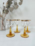 Vintage set of four shot glasses with amber stems and gilt rims, photographed on a white surface