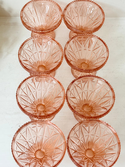 Eight pink cut-glass dessert or cocktail glasses arranged in two columns on a light off-white surface.