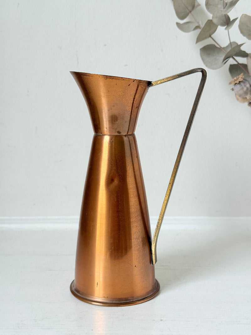 Vintage copper and brass jug with slender handle, photographed on a white surface