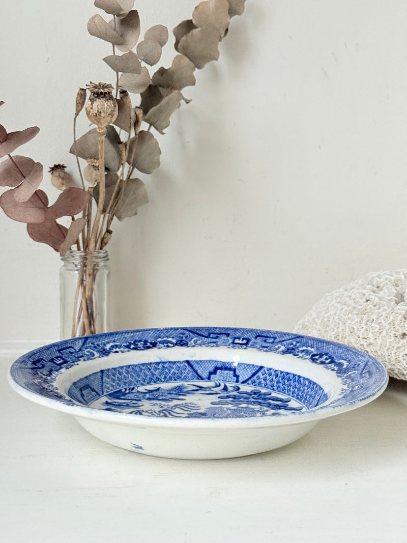 Antique Blue Willow serving bowl with cobalt transfer pattern shown on a white surface.