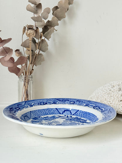 Antique Blue Willow serving bowl with cobalt transfer pattern shown on a white surface.