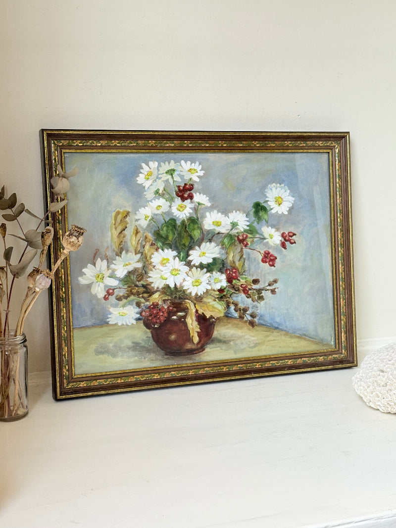 Vintage oil painting on board of daisies in a vase, framed under glass and photographed on a white surface beside dried flowers.