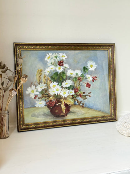 Vintage oil painting on board of daisies in a vase, framed under glass and photographed on a white surface beside dried flowers.