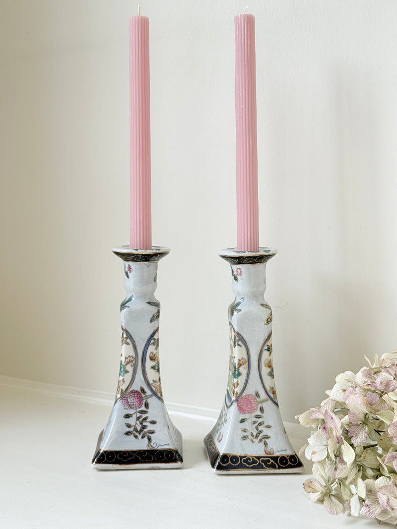 Pair of porcelain candle holders with hand-painted floral and vase motif in muted greens, pinks, and gold, styled with blush pink taper candles.