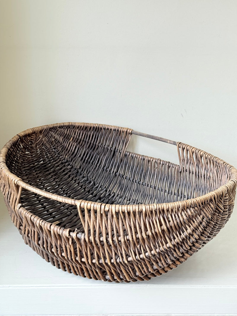 Large vintage woven basket with sculptural oval shape and integrated handles photographed on a white surface
