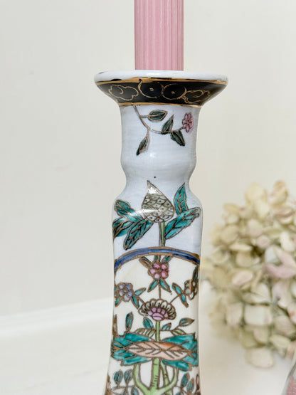 Pair of porcelain candle holders with hand-painted floral and vase motif in muted greens, pinks, and gold, styled with blush pink taper candles.