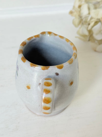 vintage studio pottery milk jug with hand painted lilac flowers and ochre rim photographed on white surface