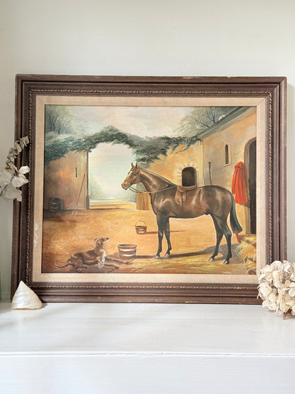 A framed vintage-style painting depicting a brown horse in a stable courtyard, displayed on a white shelf with decorative seashells against a light gray wall.