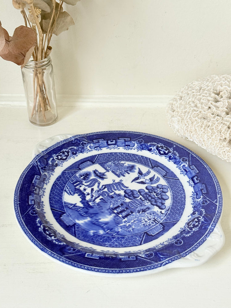 Blue Willow serving plate with scroll handled relief shown on a white surface.