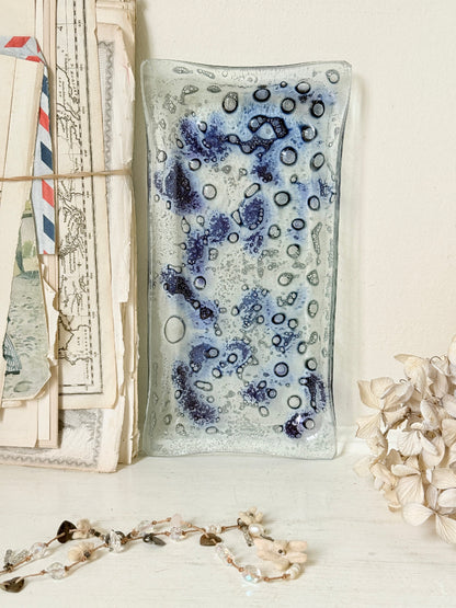 A rectangular glass dish with a textured, bubbly pattern in shades of blue, purple, and white, styled on a white surface next to vintage letters and dried flowers.