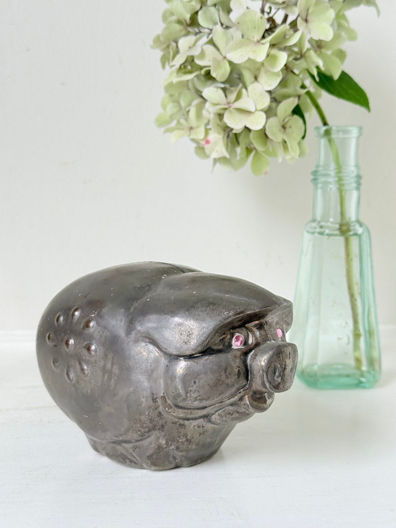 Vintage cast metal piggy bank in the shape of a pig with red painted eyes, photographed on a white surface