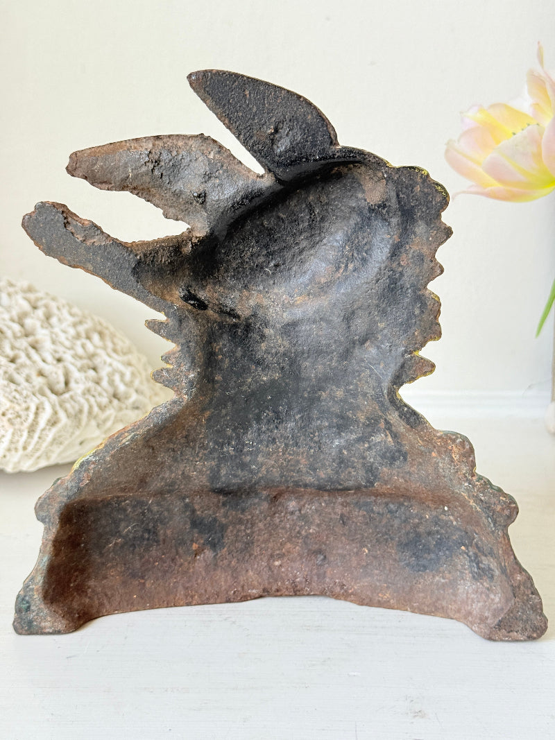 A rustic, hand-carved dark metal or stone decorative object with a textured, weathered finish, shown on a white surface with a soft-focus background.