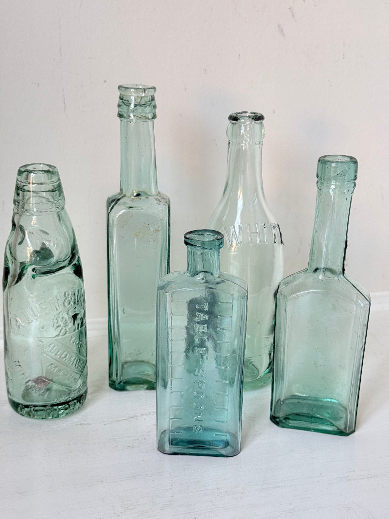 Set of five antique aqua green glass bottles with embossed lettering, photographed on a white surface