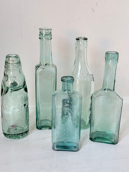 Set of five antique aqua green glass bottles with embossed lettering, photographed on a white surface