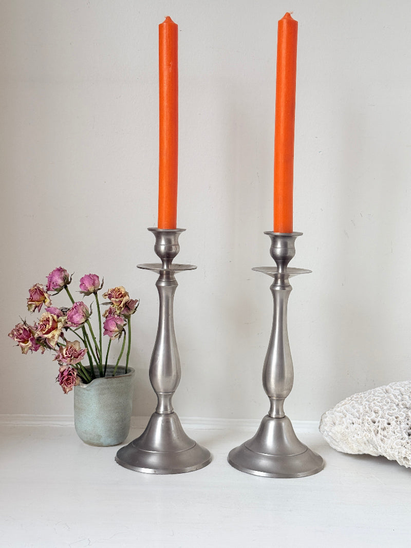 Pair of vintage pewter effect baluster candlesticks with orange taper candles styled on a white surface