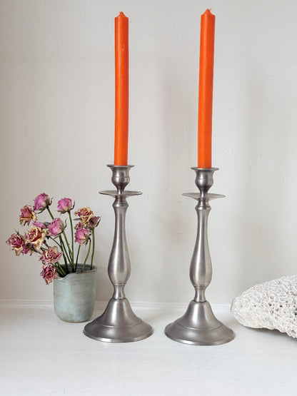 Pair of vintage pewter effect baluster candlesticks with orange taper candles styled on a white surface