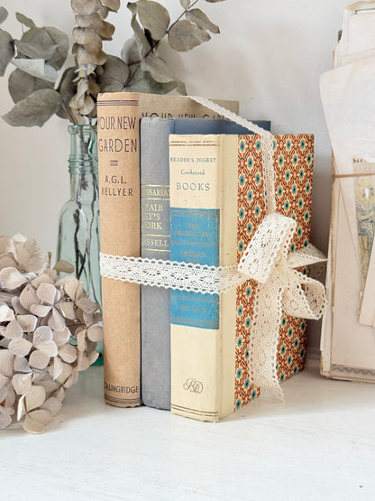 Bundle of vintage cream and blue cloth books with one patterned cover tied with ivory lace for shelf styling