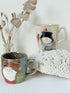 Pair of Christmas mugs with Santa and snowman designs photographed on a white surface.