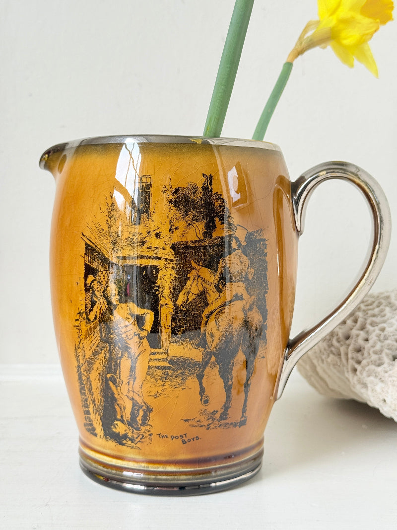Antique Ridgways stoneware jug photographed on a white surface in amber treacle glaze with black Coaching Days and Coaching Ways transfer scenes and silver tone handle