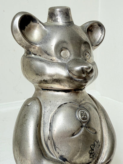 Vintage silver tone metal bear money box with coin slot on top, photographed on a white surface.