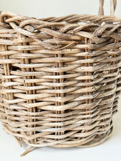 Rustic vintage wicker basket with woven handle and aged natural finish photographed on a white surface